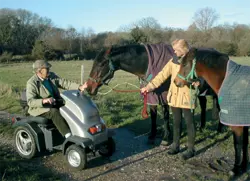 a picture of a disabled person looking at two horses close up in a field on his scooter