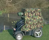 a picture of a scooter covered in a camoflage net at the side of a lake bird watching